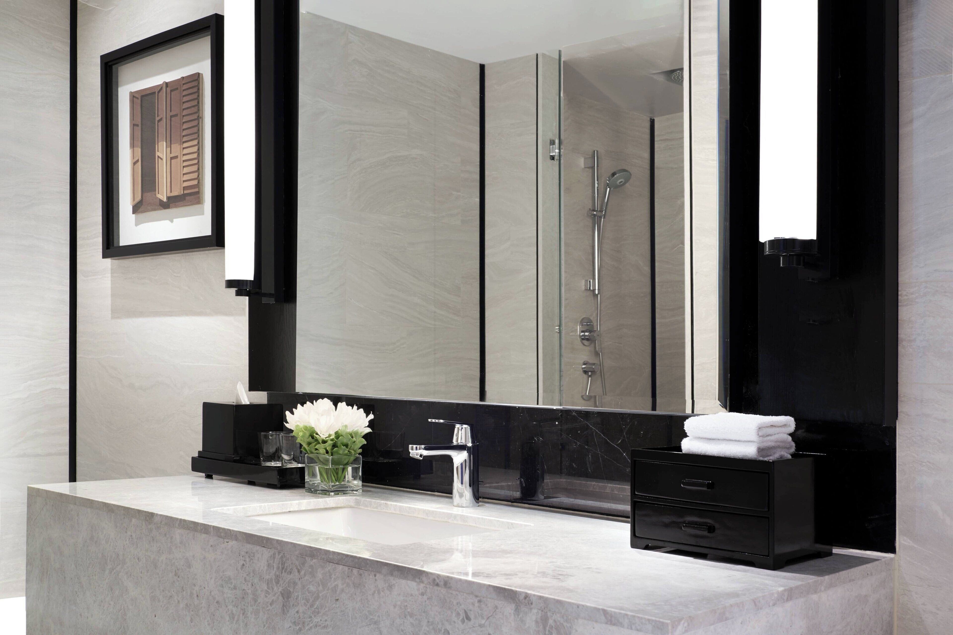 A modern bathroom with a large mirror, a marble sink, a glass shower enclosure, and a black vanity.