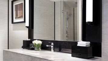 A modern bathroom with a large mirror, a marble sink, a glass shower enclosure, and a black vanity.