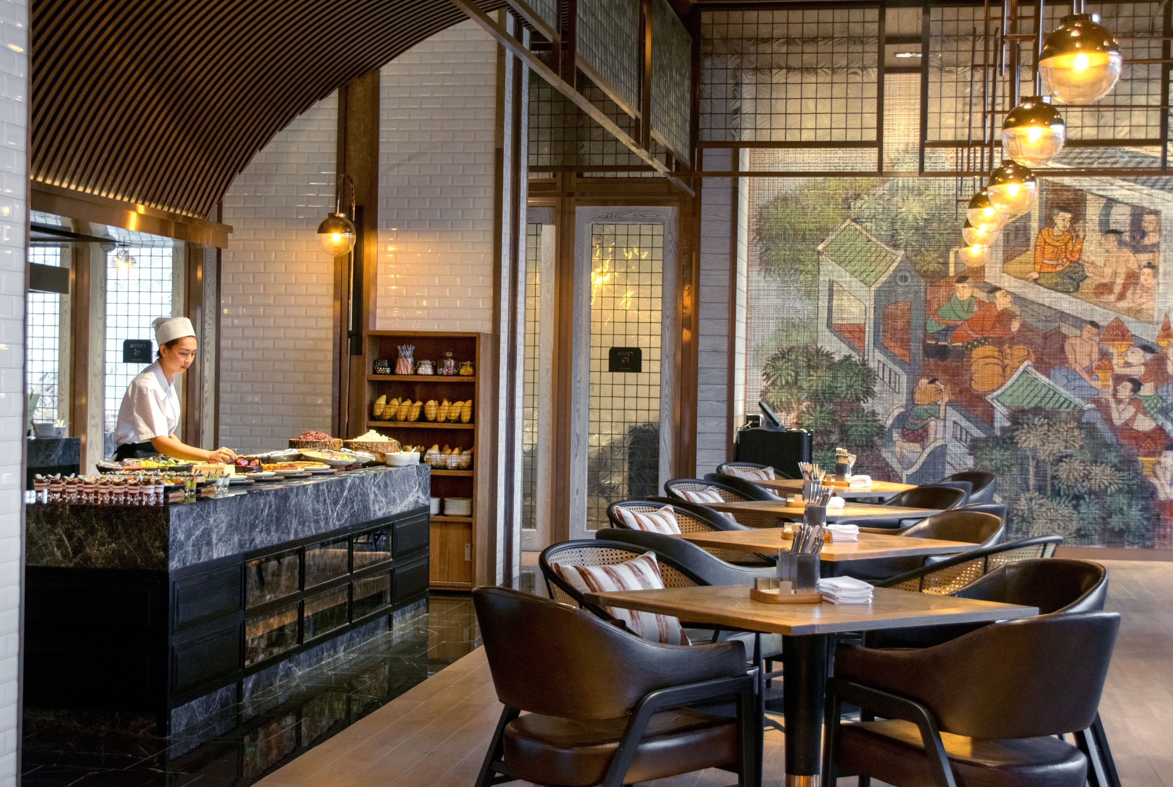 A restaurant with a chef preparing food at a marble counter, wooden tables, and a mural on the wall.