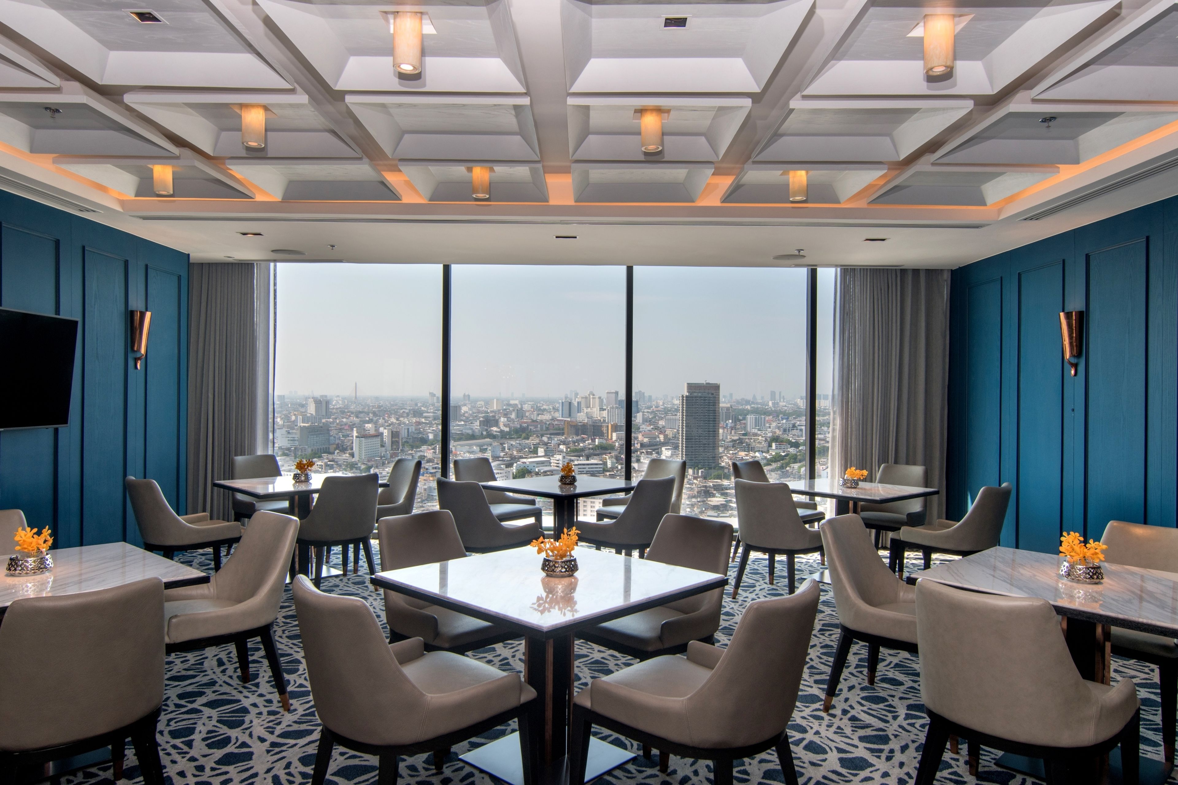 A modern hotel dining area with large windows, city views, and contemporary furniture.