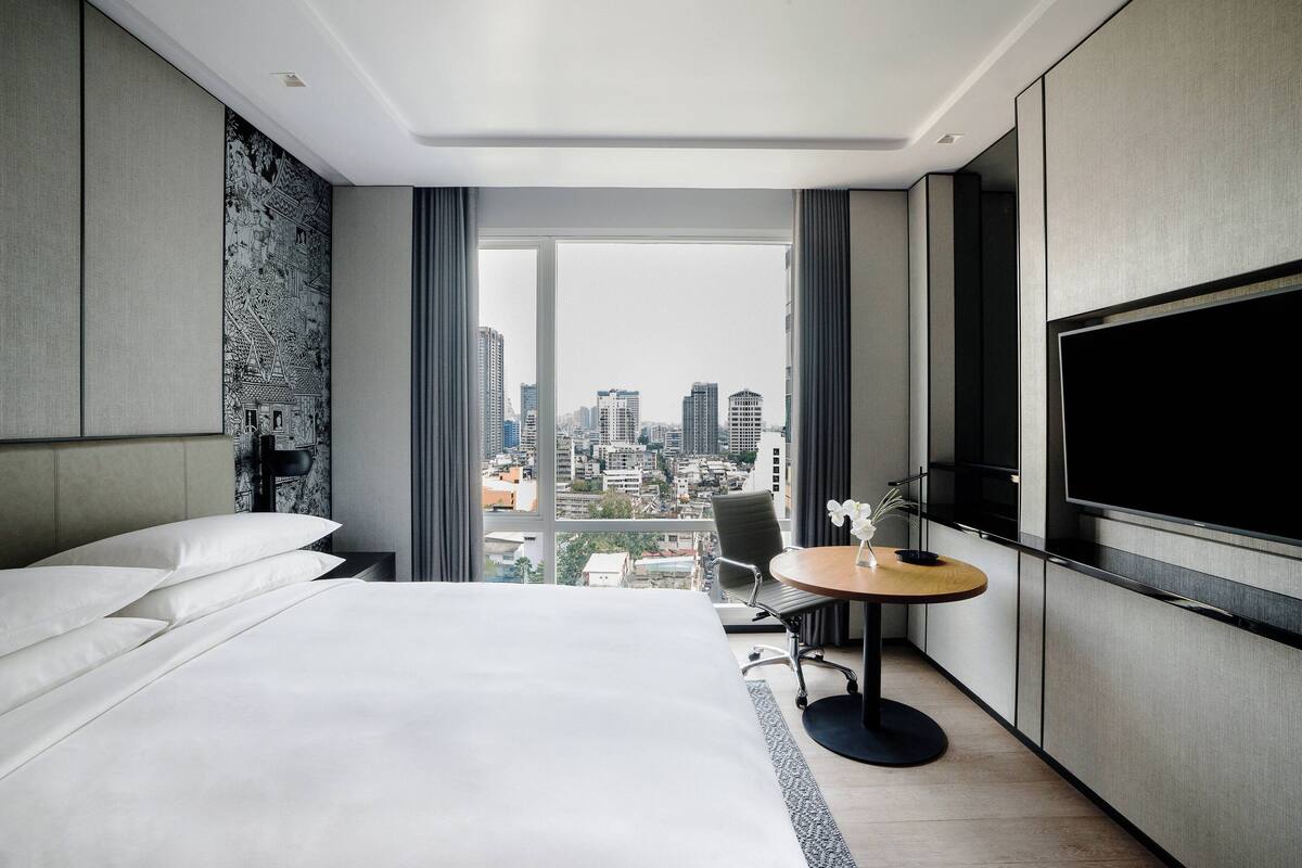 A hotel room with a large bed, a desk with a chair, a TV, and a city view.