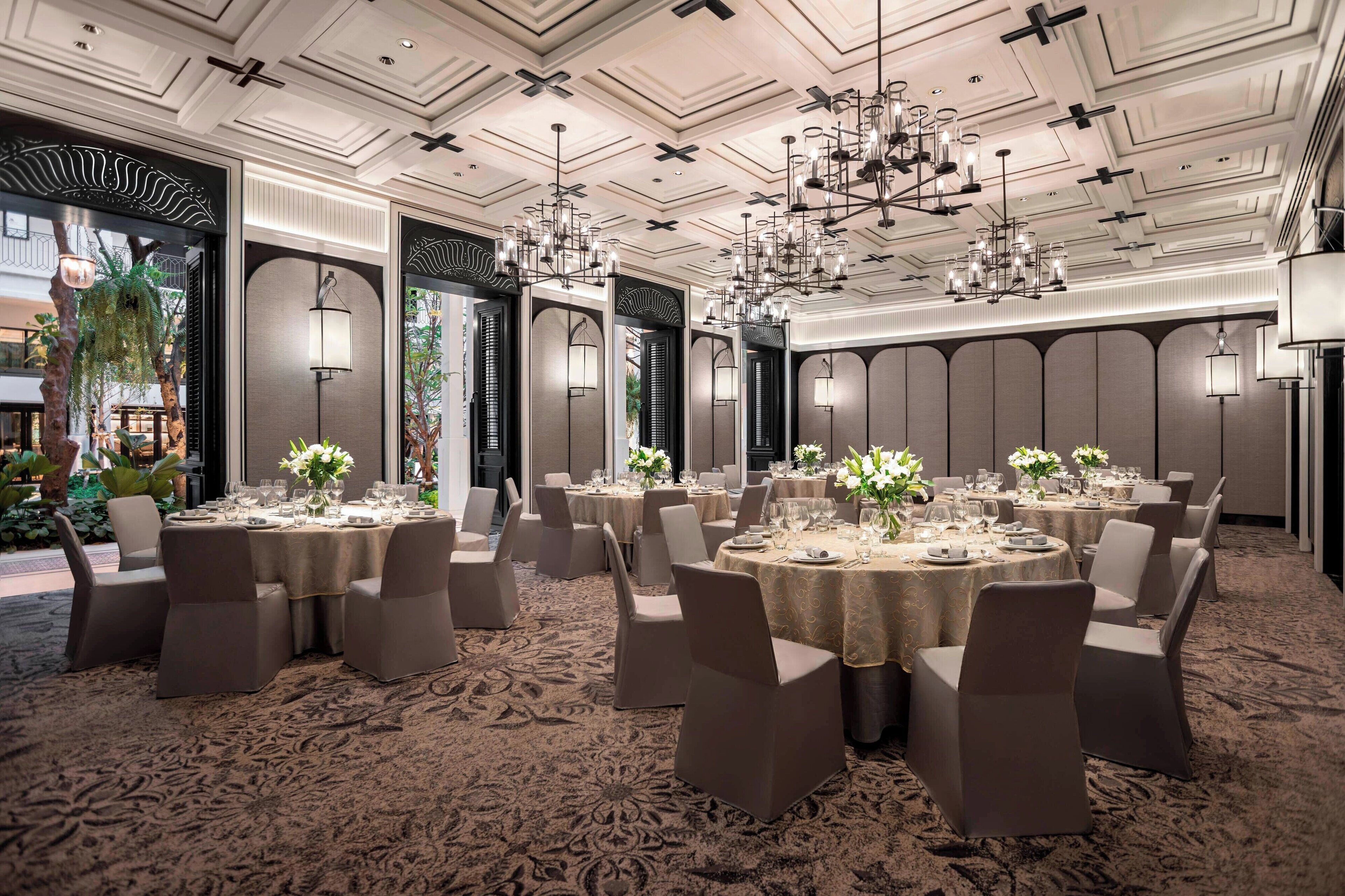 A formal dining room with round tables, chairs, and chandeliers.