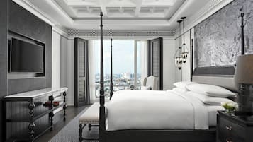 A modern hotel room with a large bed, a TV, a desk, and a view of the city.