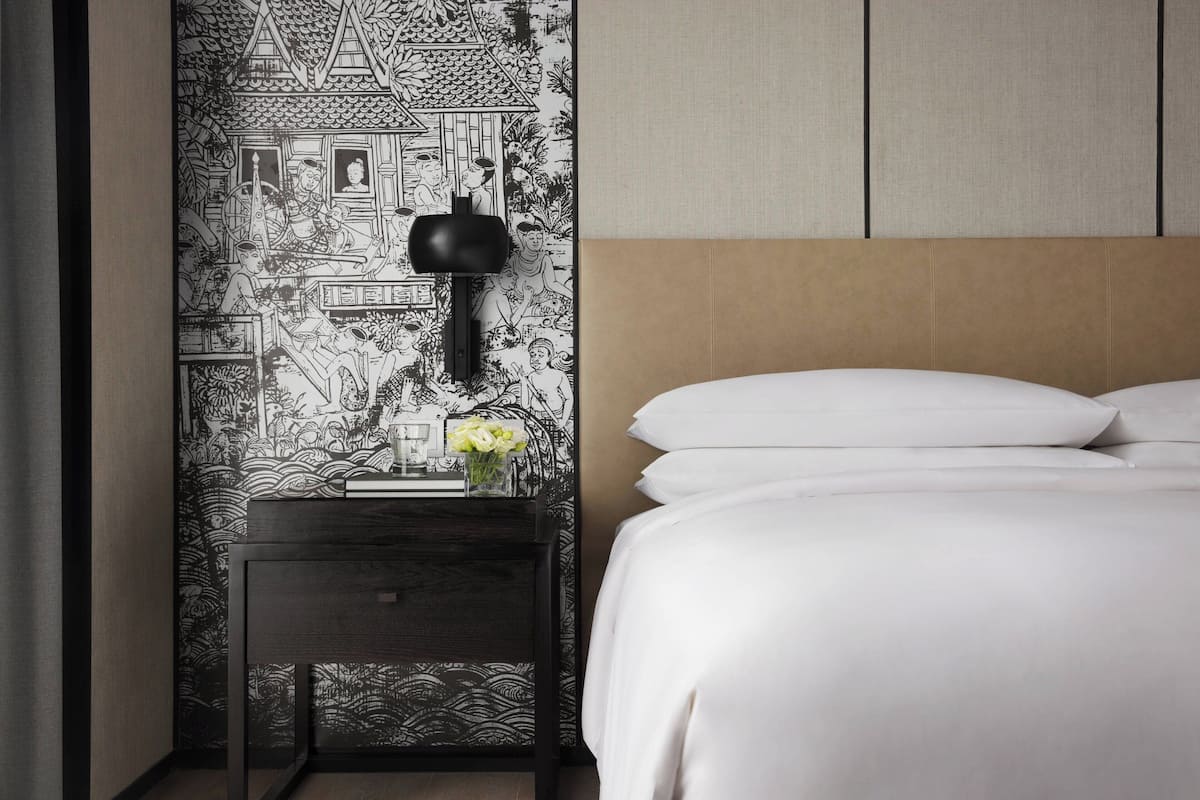 A bedroom with a bed, a nightstand with a lamp, and a wall with a black and white patterned wallpaper.