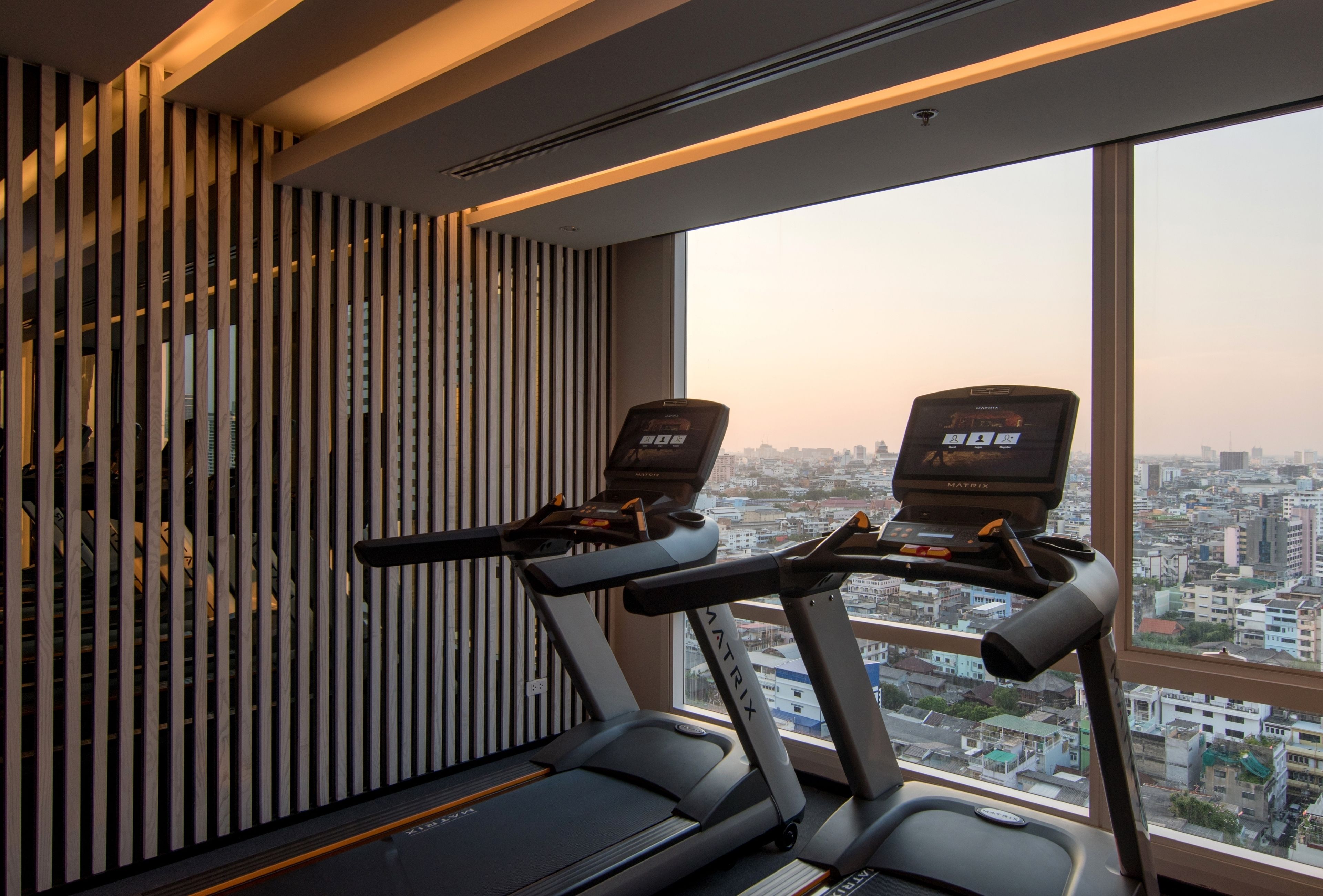 A treadmill and a stationary bike in a room with a city view through a large window.