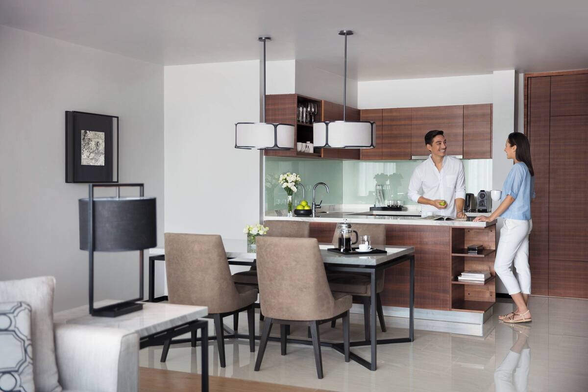 A modern kitchen with a dining area, featuring a central island, pendant lights, and wooden cabinetry.