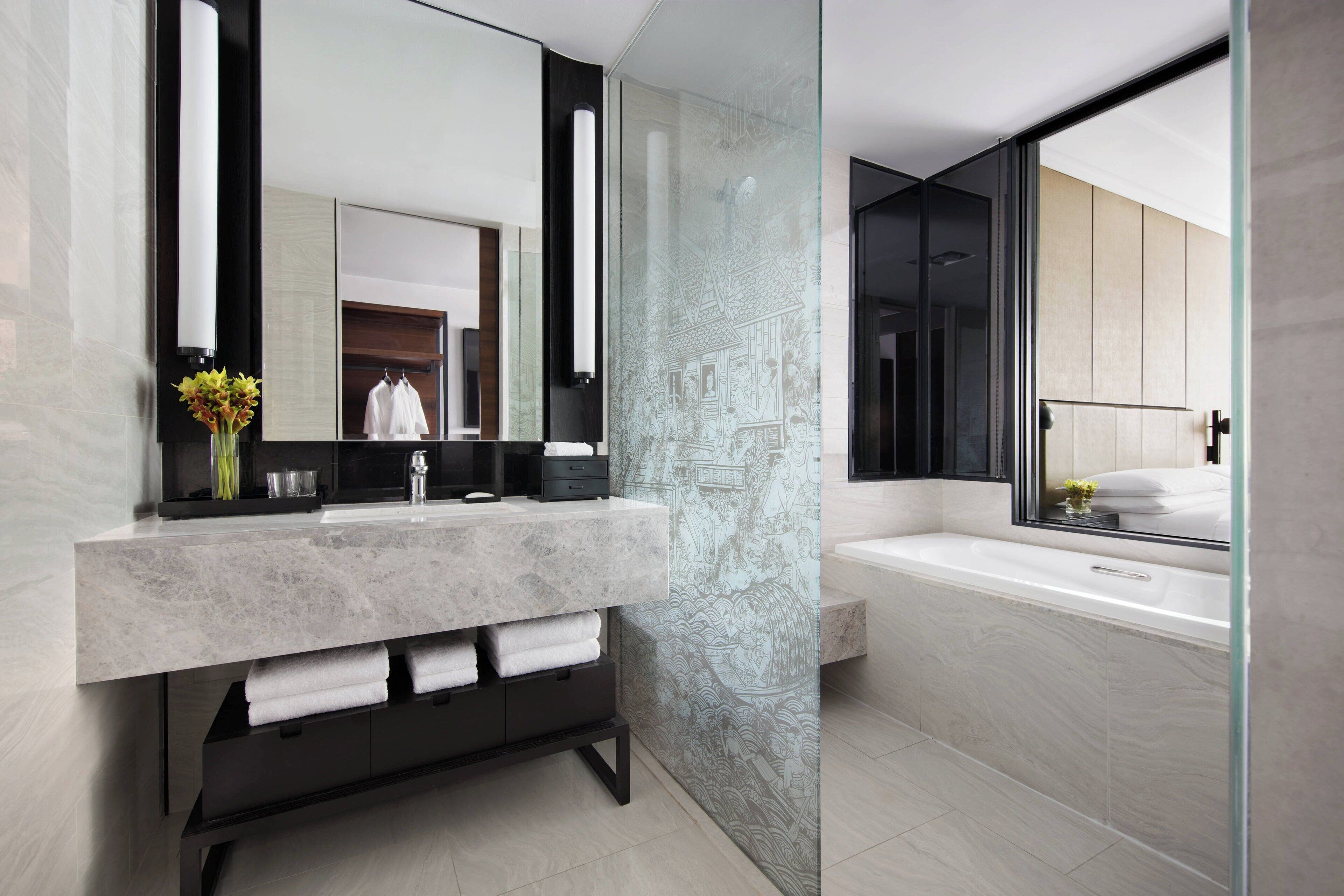 A modern bathroom with a marble vanity, a large mirror, and a bathtub.