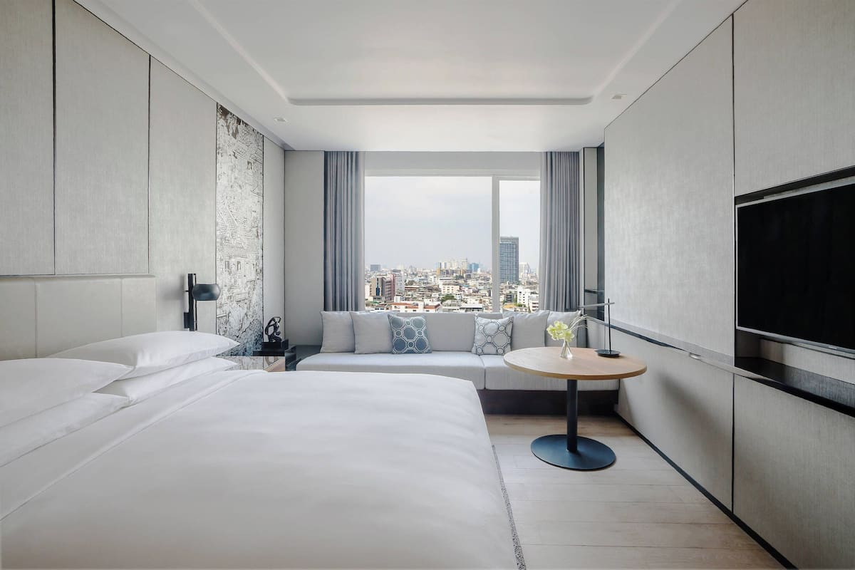 A modern hotel room with a large bed, a sofa, a round table, and a TV.