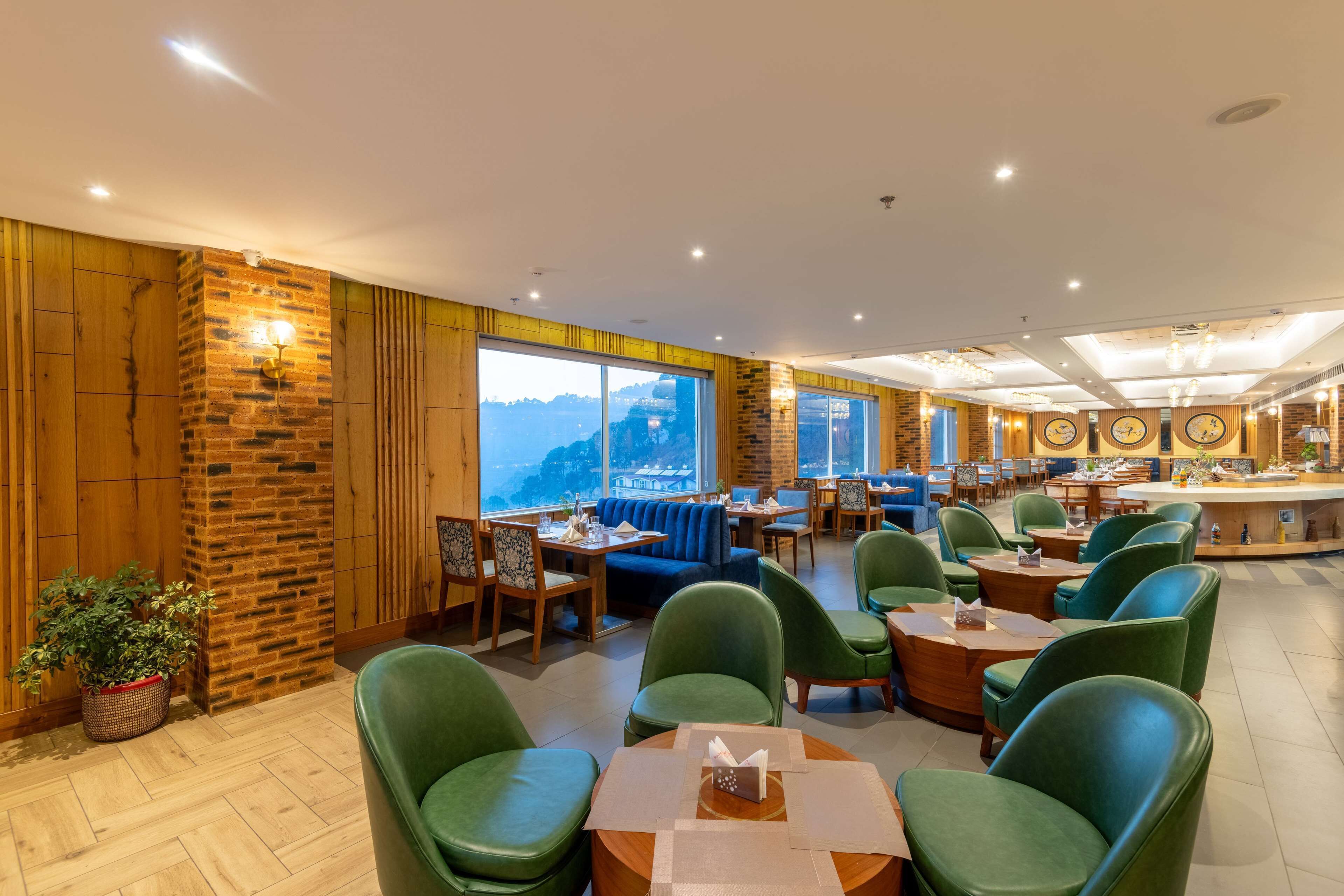 Ein Restaurant mit Backsteinwand, grünen Stühlen und Blick auf die Berge.