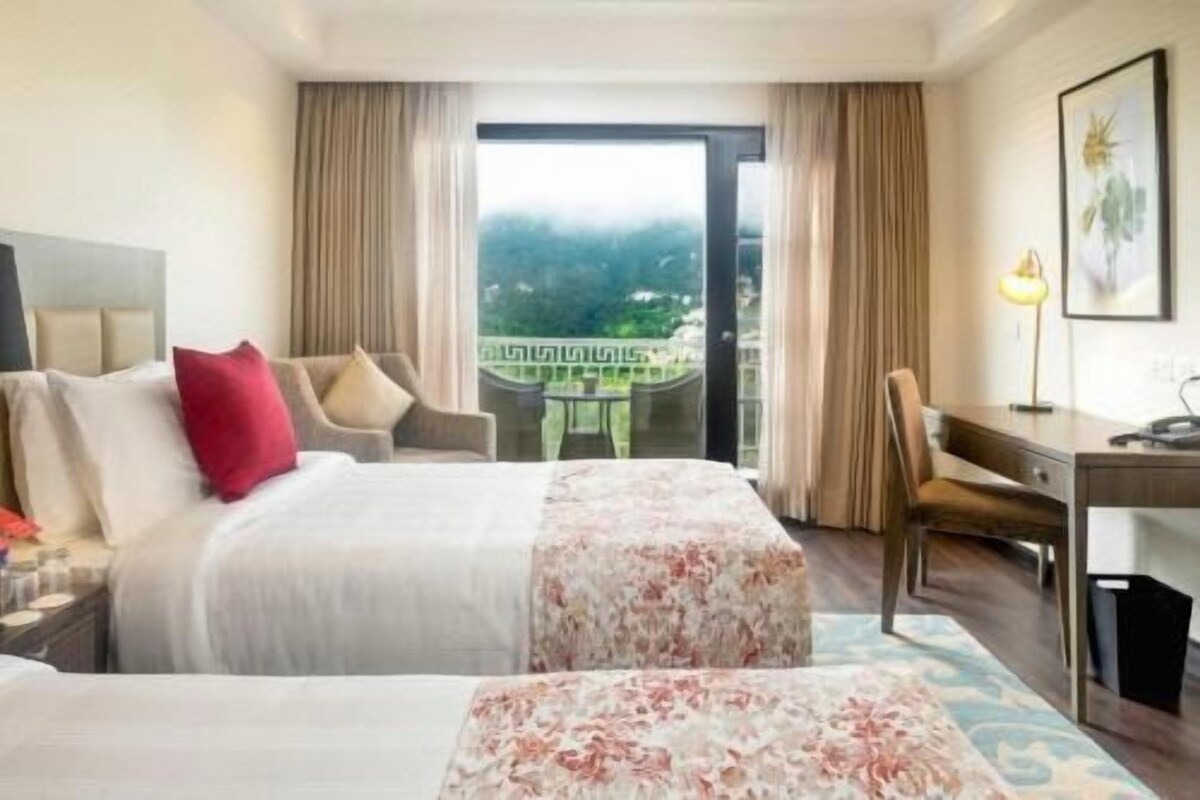 Habitación de hotel con dos camas, un escritorio y vistas a un paisaje montañoso.