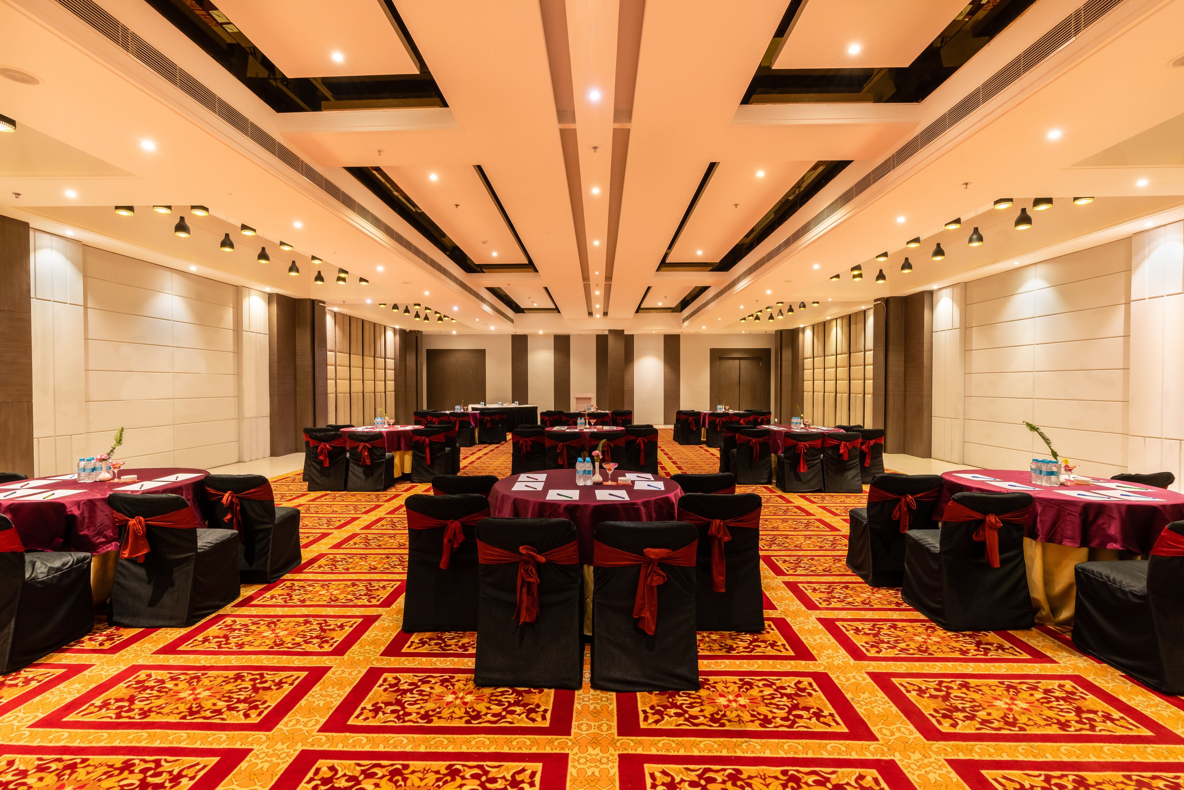 A conference room with round tables, black chairs with red sashes, and a patterned carpet.
