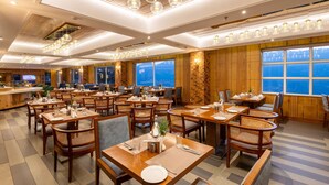 Ein Restaurant mit mehreren Tischen und Stühlen, großen Fenstern mit Blick und schwebenden, kugelförmigen Leuchten.