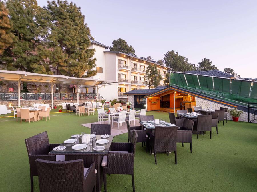 An outdoor dining area with tables and chairs, a covered seating area, and a building in the background.