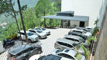 Un espace de stationnement avec plusieurs voitures, un bâtiment abrité et une vue sur des collines verdoyantes.