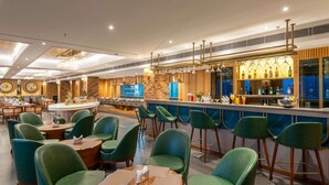 Eine moderne Bar mit grünen Barhocker, einer Theke mit verschiedenen Flaschen und einer Sitzgelegenheit mit runden Tischen und grünen Stühlen.