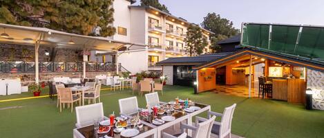 An outdoor dining area with tables and chairs, a bar, and a building with multiple balconies.