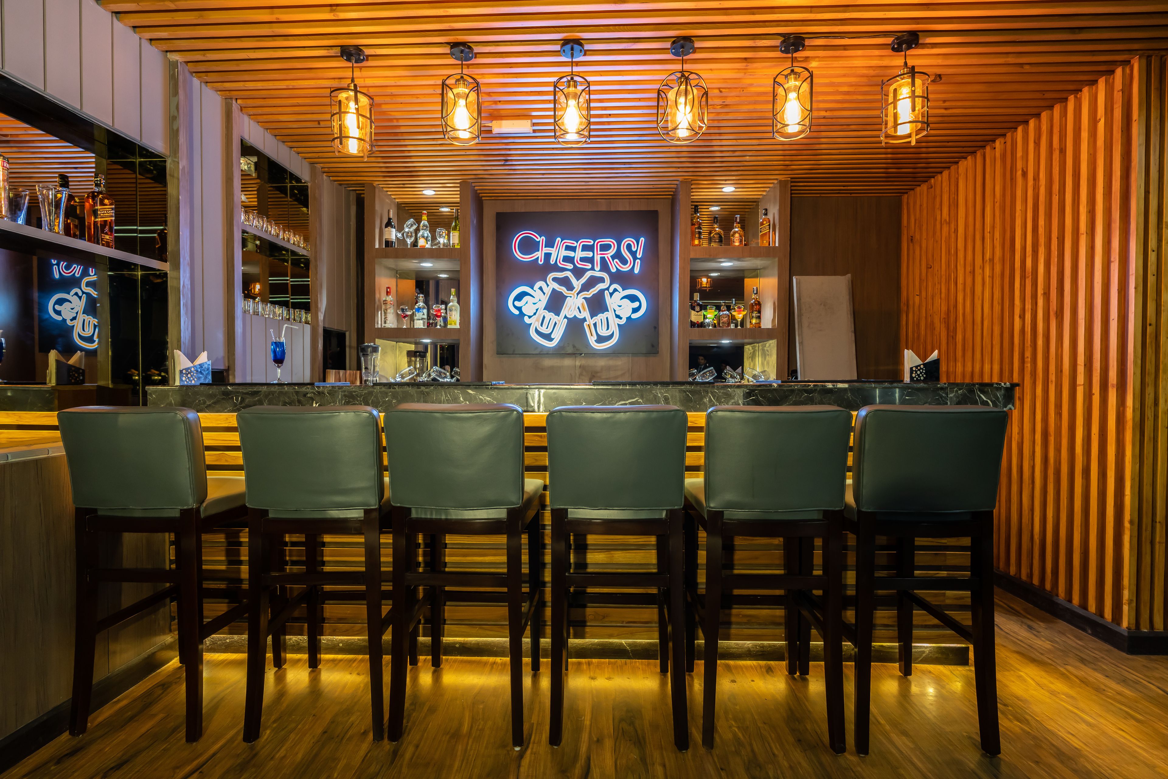 Een bar met houten plafond, barstoelen en een neonbord met de tekst 'CHEERS!'