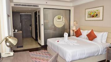 A hotel room with a bed, a desk, a chair, a desk lamp, a telephone, a mirror, and a painting on the wall.