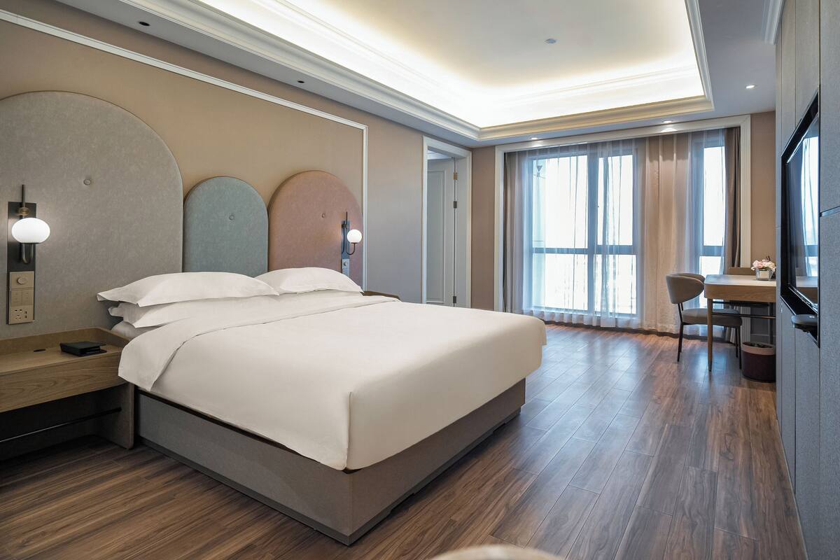 Ein modernes Hotelzimmer mit einem großen Bett, Nachttischen, einem Schreibtisch und einem Fernseher.