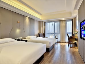A hotel room with two beds, a desk, a chair, a TV, and a large window with curtains.