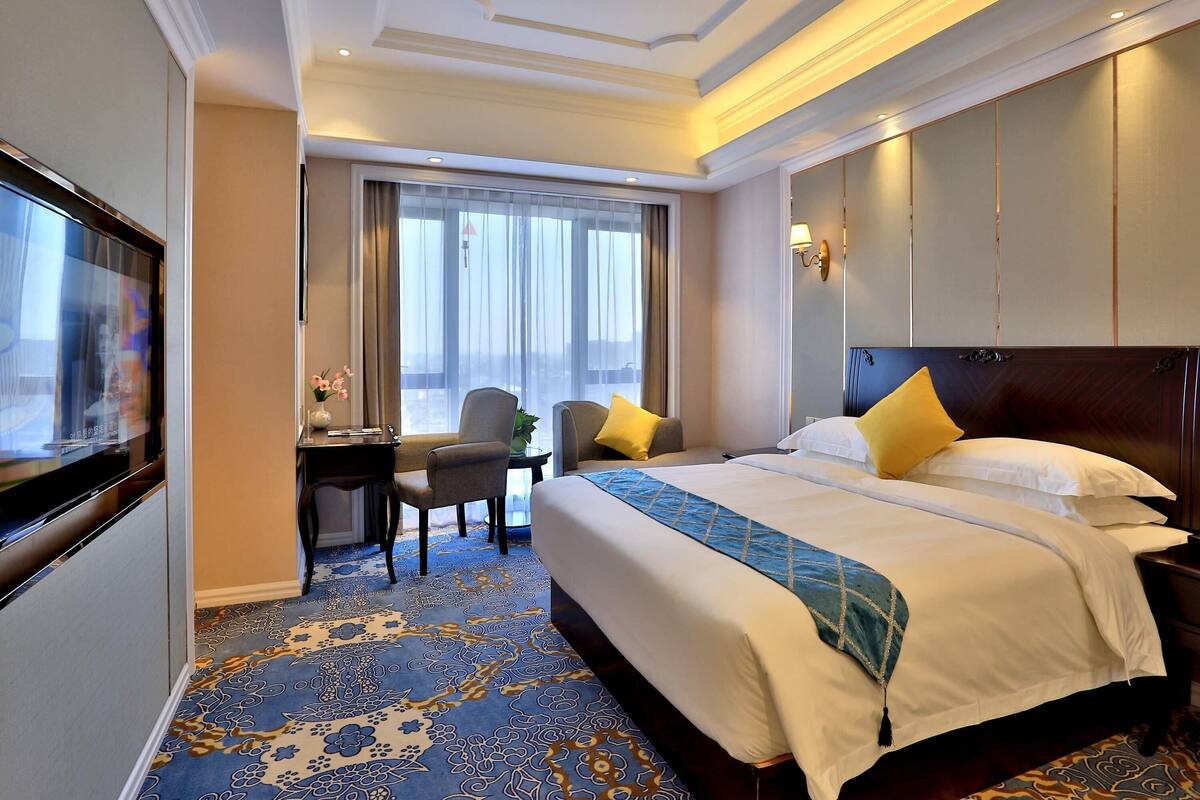 Ein Hotelzimmer mit einem großen Bett, einem Schreibtisch, einem Sessel und einem Fernseher.