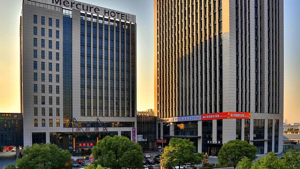Two modern high-rise buildings with commercial signage, surrounded by trees and a busy street. - Mercure Hangzhou Linping Hotel (Hangzhou)