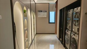 A hotel hallway with a marble floor, a row of washing machines on the right, and a wall with informational posters. - Mercure Hangzhou Linping Hotel (Hangzhou)