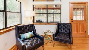 A room with two leather armchairs, a wooden desk, and a large window with a view of trees. -  Chic Hill Country Oasis (Driftwood)