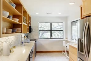 Una cocina moderna con estantes de madera, un ventanal grande y un refrigerador de acero inoxidable.