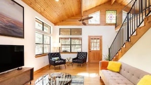 A spacious living room with a wooden ceiling, large windows, a sofa, two armchairs, a coffee table, and a television. -  Chic Hill Country Oasis (Driftwood)