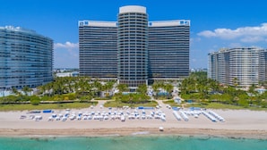 A beachfront hotel with a curved facade, multiple balconies, and a pool area with umbrellas.