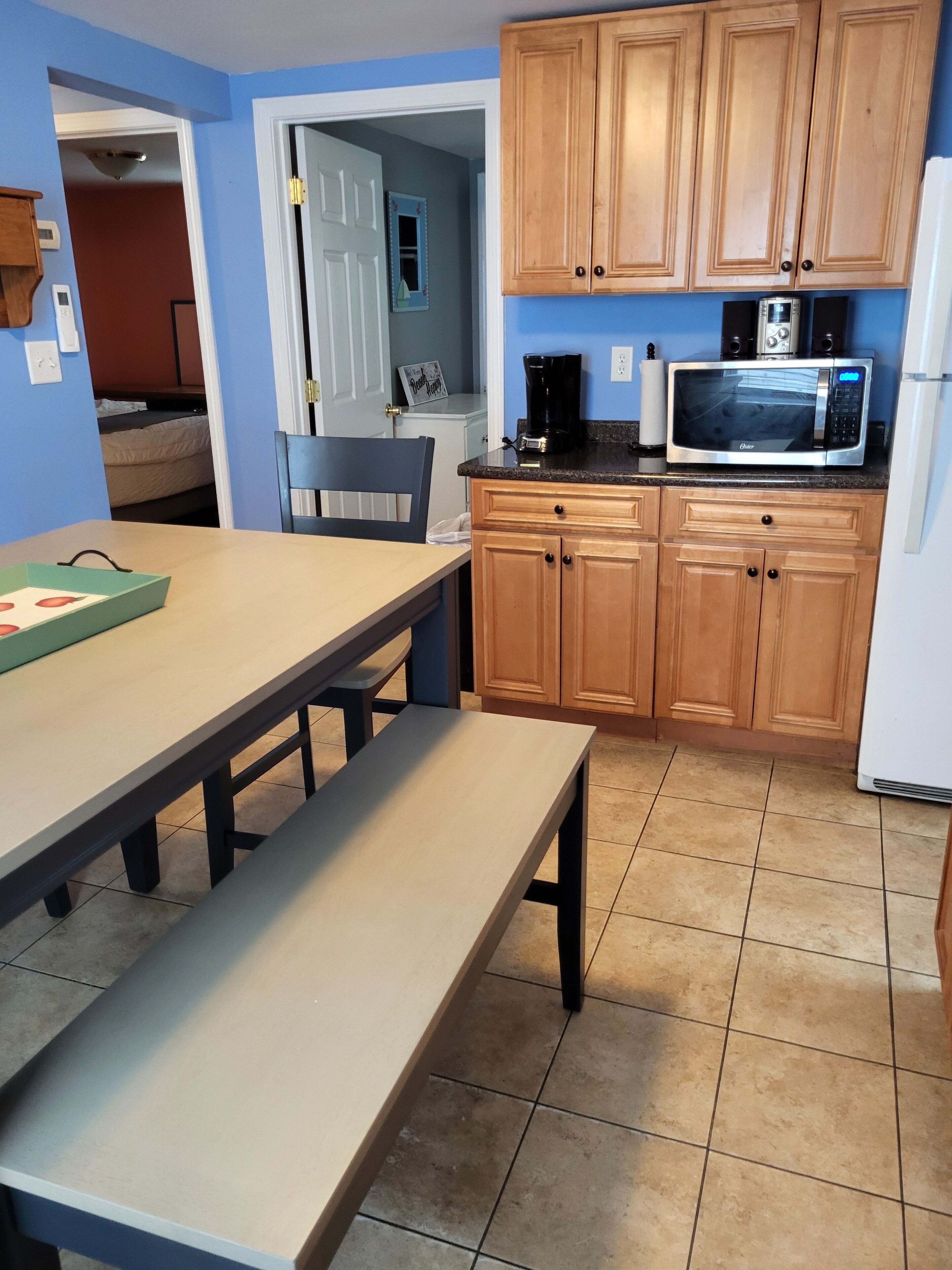 A kitchen with wooden cabinets, a microwave, and a coffee maker. There is a table with a bench, and a chair is visible.