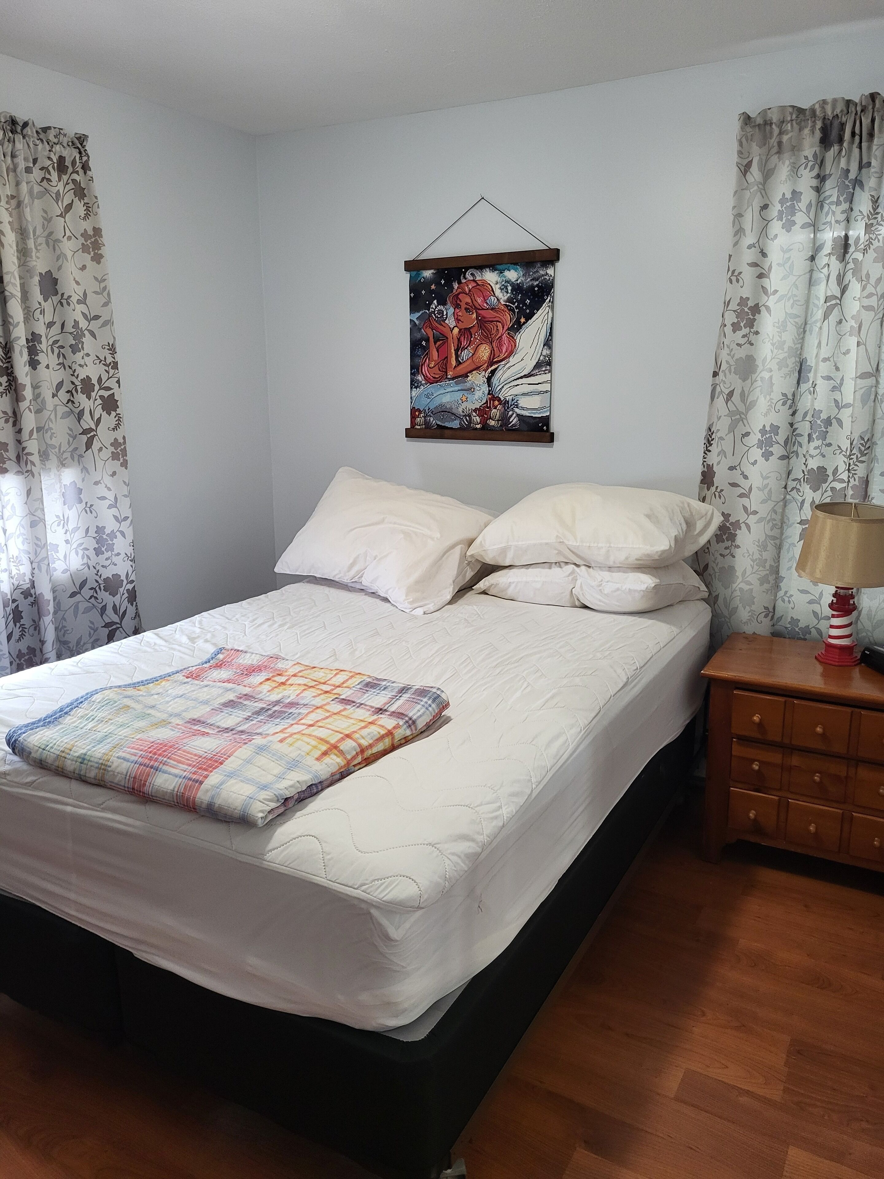 A bedroom with a bed, pillows, a quilt, a nightstand, a lamp, and a wall hanging.