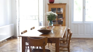 Een eetkamer met een houten tafel, stoelen, een vaas met bloemen en een houten kast op de achtergrond.
