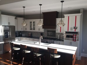 A modern kitchen with a central island, bar stools, stainless steel appliances, and pendant lighting.