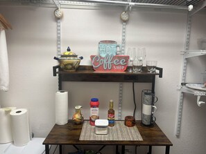 Un coin cuisine avec une étagère sur laquelle sont posés une enseigne de café, un pot décoratif et divers ustensiles de cuisine.