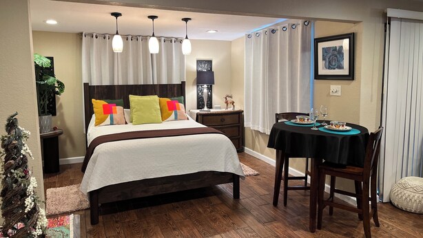 Een hotelkamer met een bed, nachtkastje, lamp en een zithoek met een tafel en stoelen.