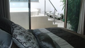 Un dormitorio con una cama, vistas a un balcón con mesa y sillas, y una escalera que da al exterior.