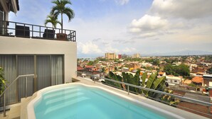 Piscina en la azotea con vistas a un paisaje urbano, que incluye palmeras y edificios.