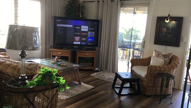 A living room with a flat-screen TV, wicker furniture, a ceiling fan, and a view of the outdoors.