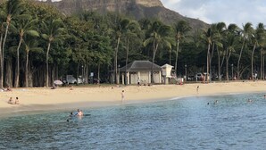 A beach with palm trees, a lifeguard tower, and a mountain in the background.