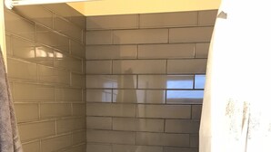 A small, dark-tiled shower area with a towel hanging on the wall, a shower curtain, and two bottles of shampoo. - STUDIO AWESOMENESS FOR YOU LMU SILICON BCH VENICE (Los Angeles)
