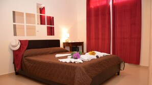 Una cama bien hecha con una colcha marrón, un sombrero blanco y toallas sobre la cama.