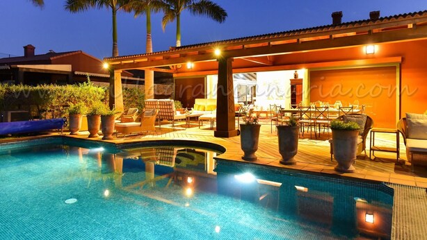 A pool area with lounge chairs and a dining area, surrounded by palm trees. - Villa La Canela by VillaGranCanaria (San Bartolomé de Tirajana)