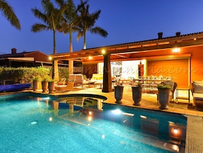 A pool area with lounge chairs and a dining area, surrounded by palm trees. - Villa La Canela by VillaGranCanaria (San Bartolomé de Tirajana)