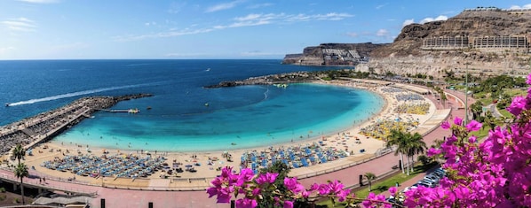 A coastal beach with a curved shoreline, a promenade, and a cliffside building. - Villa La Canela by VillaGranCanaria (San Bartolomé de Tirajana)