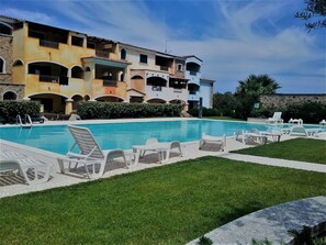 Une piscine entourée de chaises longues blanches, avec un bâtiment doté de nombreux balcons en arrière-plan.