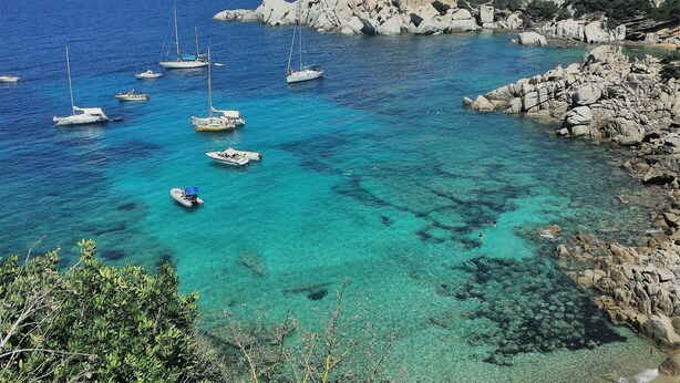 Una zona costera con barcos fondeados cerca de costas rocosas.