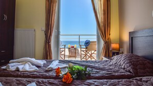 A hotel room with a bed, a view of the sea through a balcony, and a table with chairs outside.