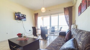 A living room with a sofa, a coffee table, a TV, and a balcony with a dining area.